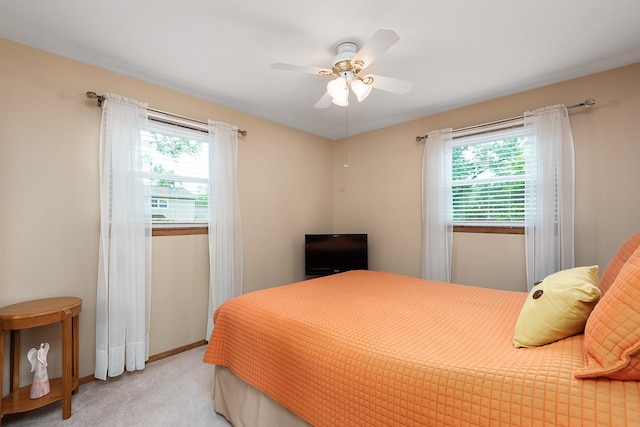 bedroom featuring a ceiling fan, light colored carpet, multiple windows, and baseboards