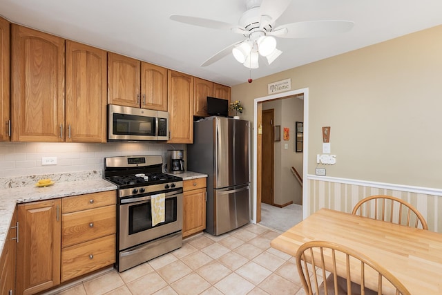 kitchen with light tile patterned floors, ceiling fan, appliances with stainless steel finishes, brown cabinets, and backsplash