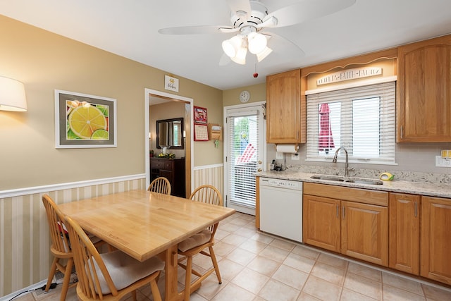 kitchen with a ceiling fan, wainscoting, light stone countertops, white dishwasher, and a sink