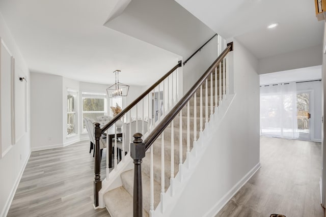 stairs with an inviting chandelier, baseboards, and wood finished floors