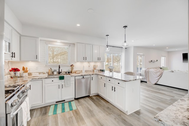 kitchen with a peninsula, white cabinets, stainless steel dishwasher, light stone countertops, and gas stove