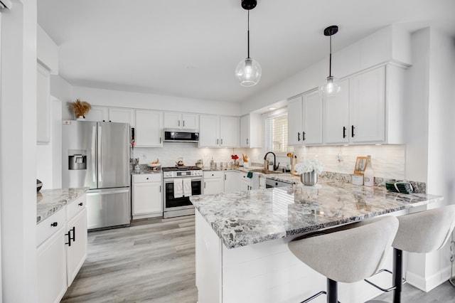 kitchen with light stone counters, a peninsula, white cabinets, appliances with stainless steel finishes, and tasteful backsplash