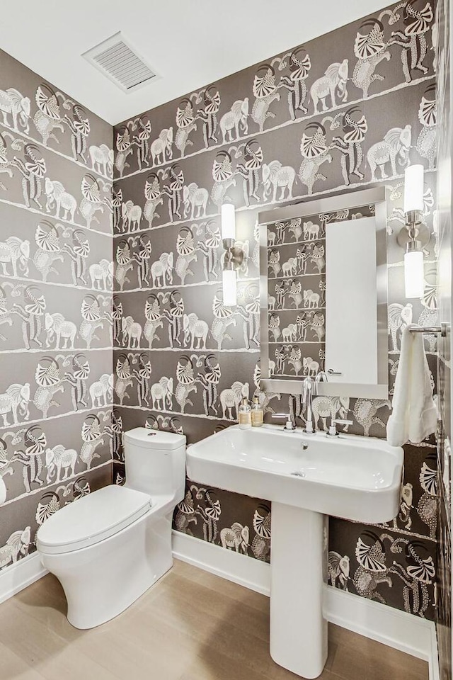 half bath with visible vents, baseboards, toilet, and wallpapered walls