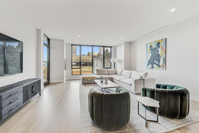 living room featuring light wood finished floors, recessed lighting, a wall of windows, and baseboards