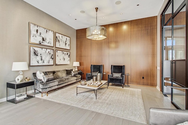 living room featuring baseboards, wood walls, recessed lighting, wood finished floors, and a notable chandelier