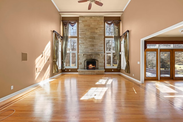 unfurnished living room with a stone fireplace, ornamental molding, wood finished floors, and baseboards