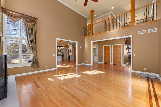 unfurnished living room featuring ceiling fan with notable chandelier, wood finished floors, visible vents, baseboards, and ornamental molding