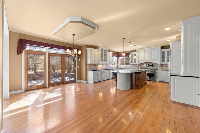 kitchen featuring a kitchen island with sink, a notable chandelier, appliances with stainless steel finishes, backsplash, and dark countertops