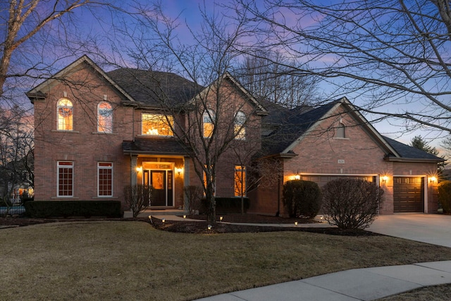 traditional-style home with a garage, concrete driveway, brick siding, and a yard