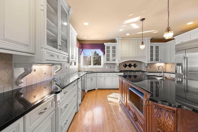 kitchen featuring built in appliances, light wood-type flooring, a sink, and decorative light fixtures