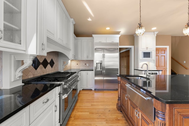 kitchen featuring light wood-style floors, high end appliances, dark stone countertops, and white cabinets