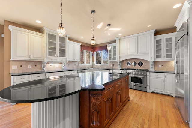 kitchen with high end appliances, light wood-type flooring, a kitchen island with sink, and a sink