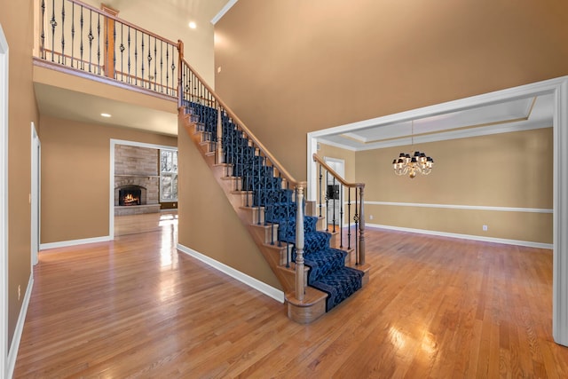 staircase with a chandelier, a fireplace, wood finished floors, baseboards, and ornamental molding