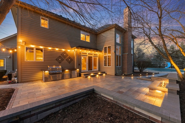 back of house with a chimney, a patio area, a fire pit, and an outdoor kitchen