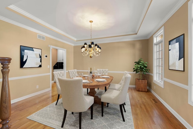 dining space featuring light wood finished floors, baseboards, visible vents, and a tray ceiling