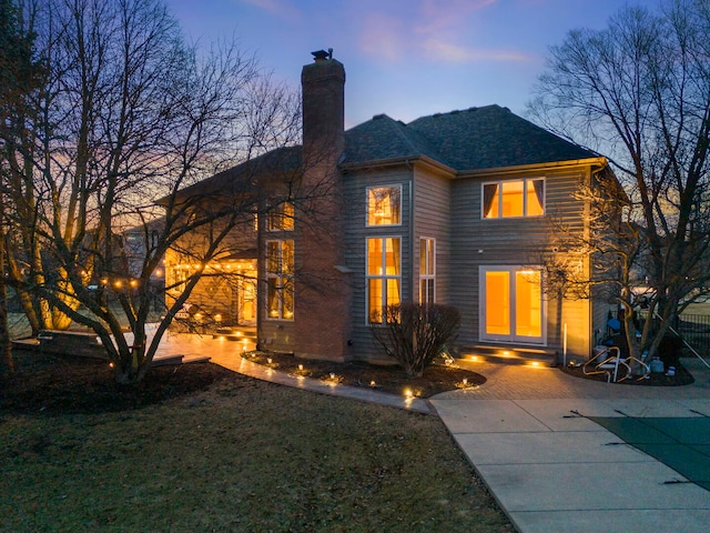 exterior space featuring a patio area, a shingled roof, a chimney, and a front yard