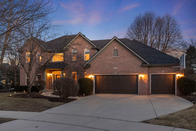 traditional-style house featuring driveway, an attached garage, a shingled roof, and brick siding