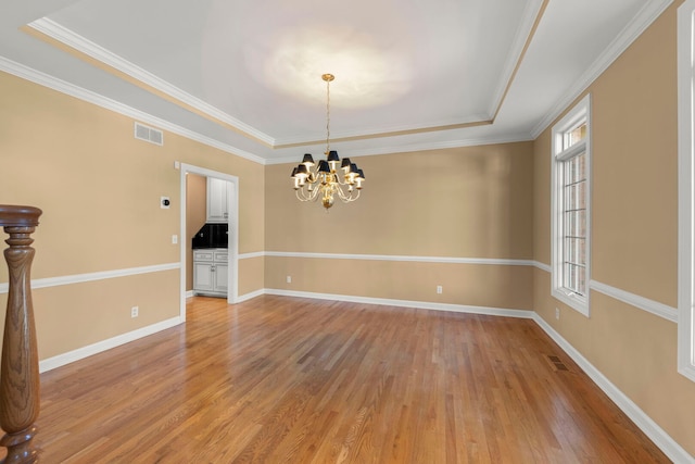 unfurnished room featuring a tray ceiling, light wood finished floors, and visible vents