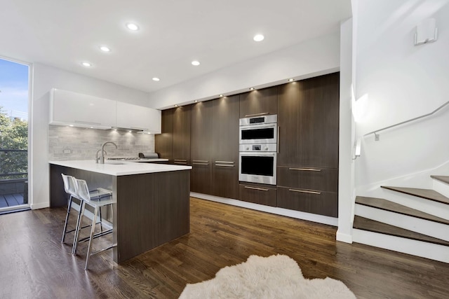 kitchen featuring double oven, a breakfast bar area, a peninsula, a sink, and modern cabinets