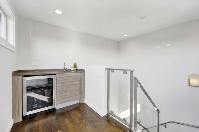 bar featuring dark wood-style flooring, recessed lighting, wet bar, beverage cooler, and baseboards