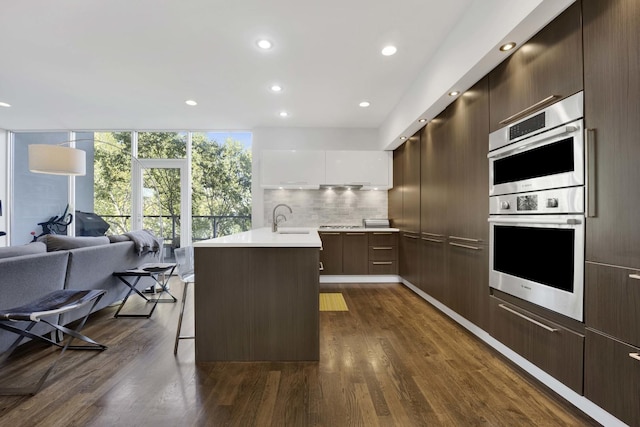 kitchen with double oven, a sink, light countertops, modern cabinets, and dark wood finished floors