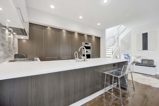 kitchen with stainless steel appliances, light countertops, dark wood-type flooring, modern cabinets, and a peninsula