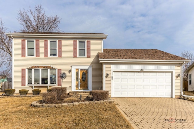 colonial-style house with a garage, roof with shingles, a front lawn, and decorative driveway