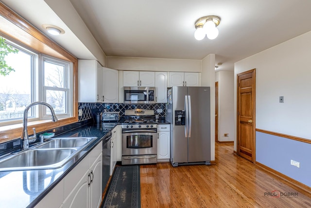 kitchen featuring dark countertops, appliances with stainless steel finishes, a sink, white cabinetry, and backsplash