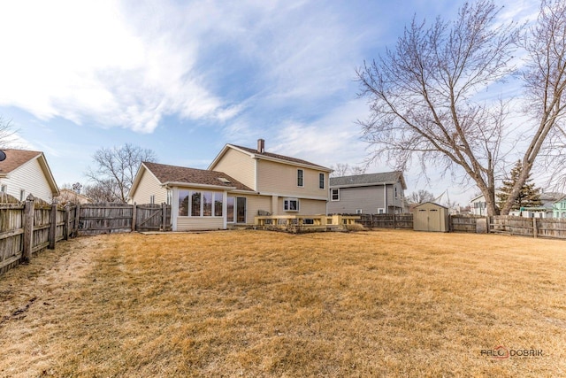 rear view of house featuring an outbuilding, a chimney, a lawn, a storage shed, and a fenced backyard