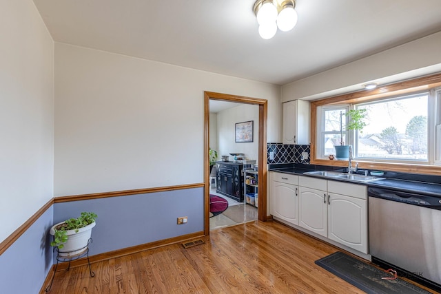 kitchen featuring a sink, visible vents, dishwasher, light wood finished floors, and dark countertops