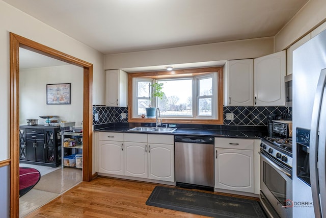 kitchen with a sink, white cabinetry, appliances with stainless steel finishes, light wood finished floors, and dark countertops