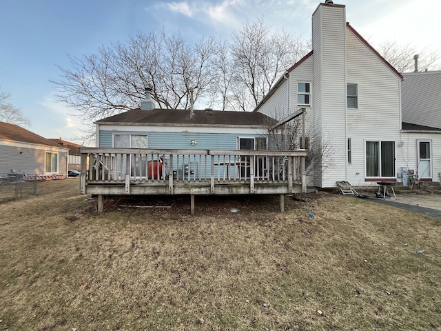 back of property featuring a chimney, a deck, and a lawn