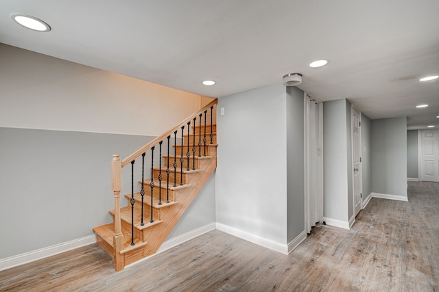 staircase featuring baseboards, wood finished floors, and recessed lighting