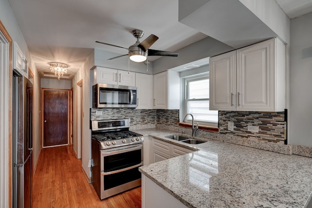 kitchen featuring light wood finished floors, stainless steel appliances, white cabinets, a sink, and light stone countertops