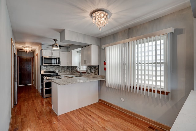 kitchen with stainless steel appliances, light wood-style flooring, white cabinetry, a sink, and a peninsula