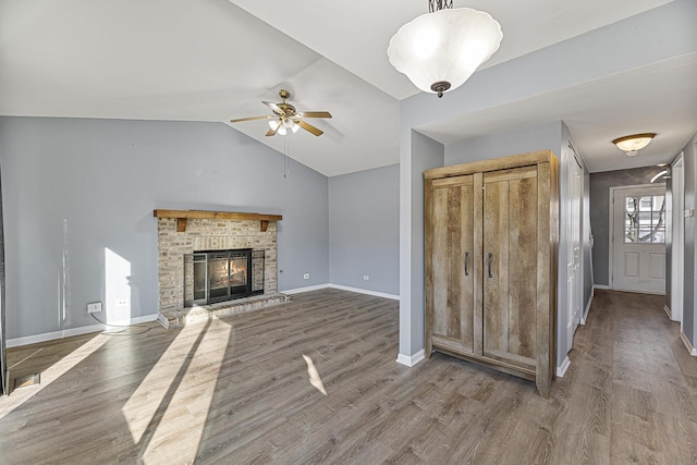 unfurnished living room with lofted ceiling, a brick fireplace, baseboards, and wood finished floors