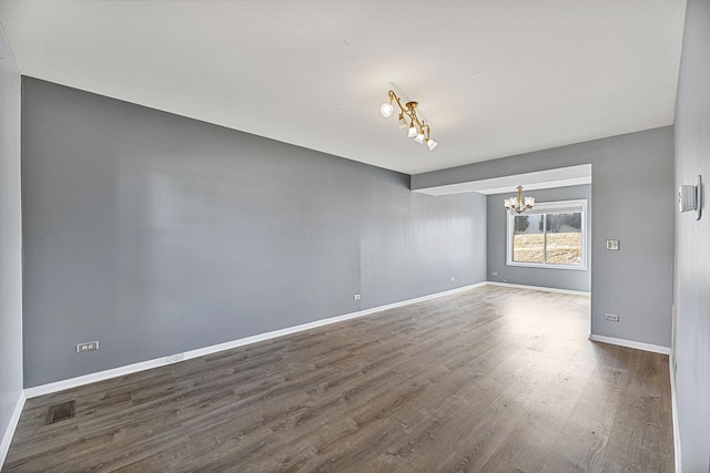 unfurnished room with a chandelier, wood finished floors, visible vents, and baseboards