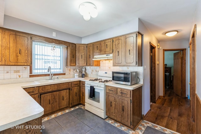 kitchen featuring brown cabinets, white gas range, stainless steel microwave, a sink, and under cabinet range hood