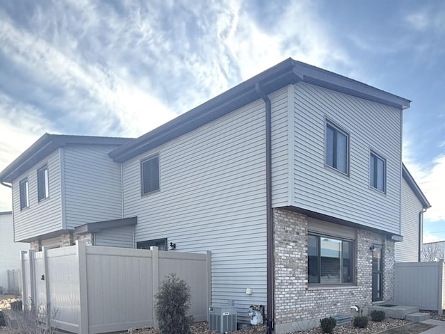 view of side of home with brick siding, central air condition unit, and fence