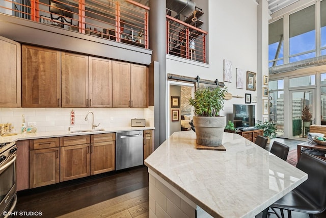 kitchen with a towering ceiling, a barn door, appliances with stainless steel finishes, and a sink