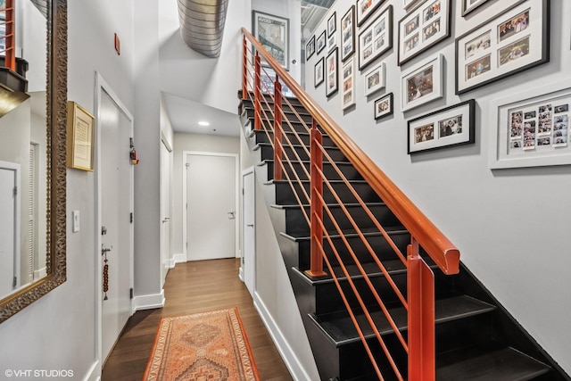 stairs featuring a high ceiling, baseboards, and wood finished floors