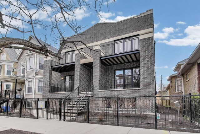 view of front of property with covered porch, brick siding, a balcony, and a fenced front yard