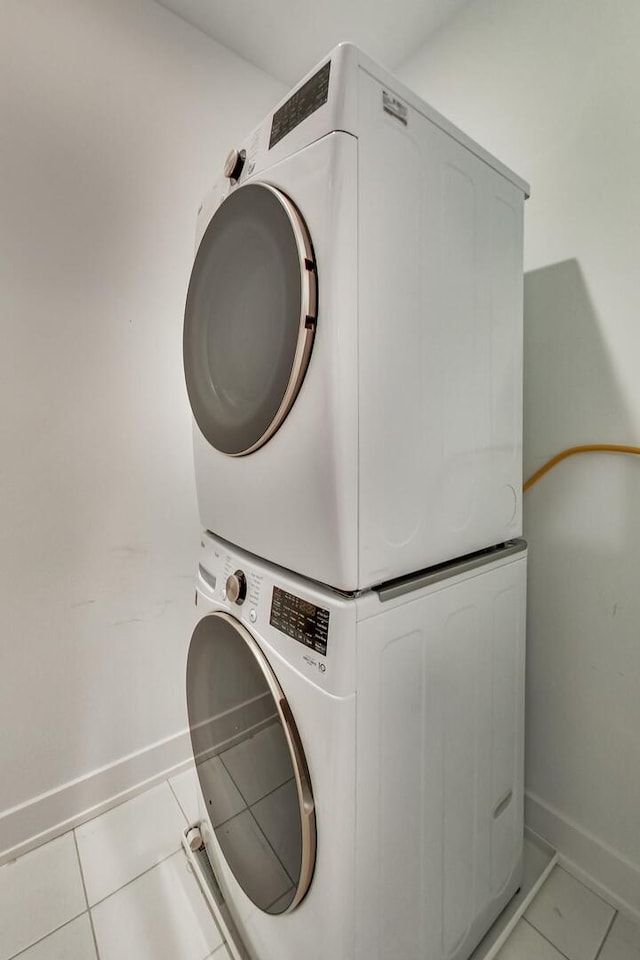 laundry area featuring laundry area, baseboards, stacked washer / drying machine, and light tile patterned flooring