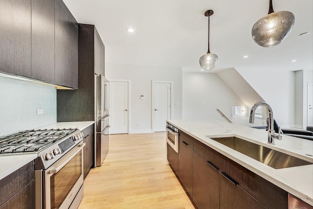 kitchen with decorative light fixtures, light wood finished floors, stainless steel appliances, a sink, and dark brown cabinets