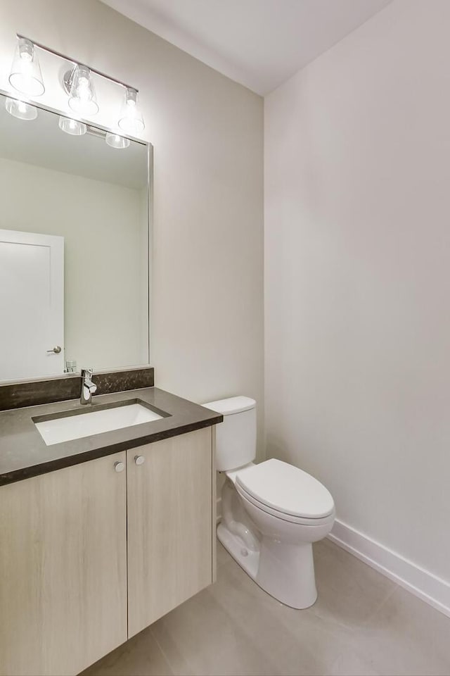 half bathroom with baseboards, vanity, toilet, and tile patterned floors