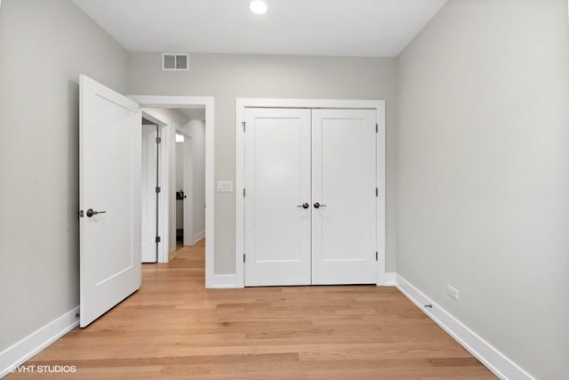 unfurnished bedroom with a closet, light wood-type flooring, visible vents, and baseboards