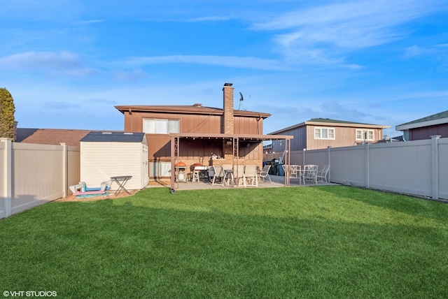 back of property with a patio, a yard, a chimney, and a fenced backyard