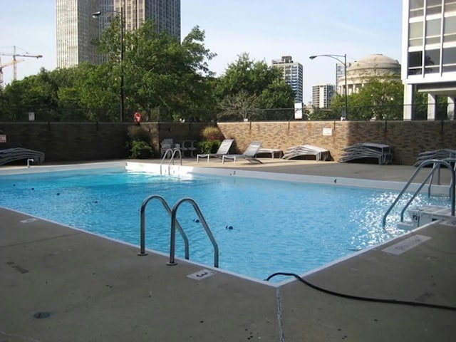 community pool featuring a city view, a patio area, and fence