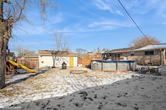 snowy yard with an outbuilding, a covered pool, a playground, and fence