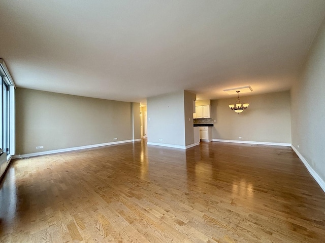 unfurnished living room with baseboards, wood finished floors, and a notable chandelier